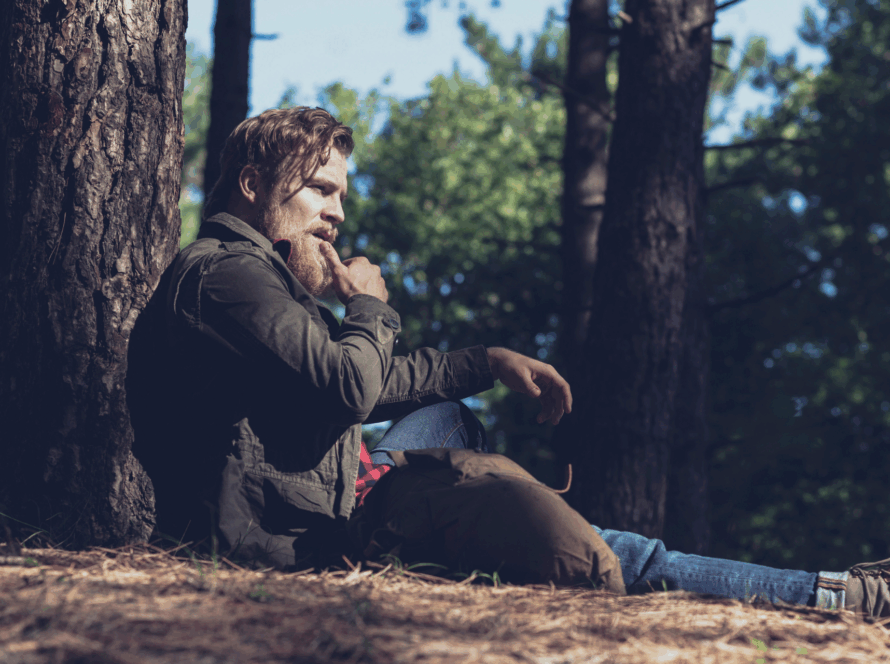 Man sitting against a tree in a forest, deep in thought, symbolising reflection and self-awareness