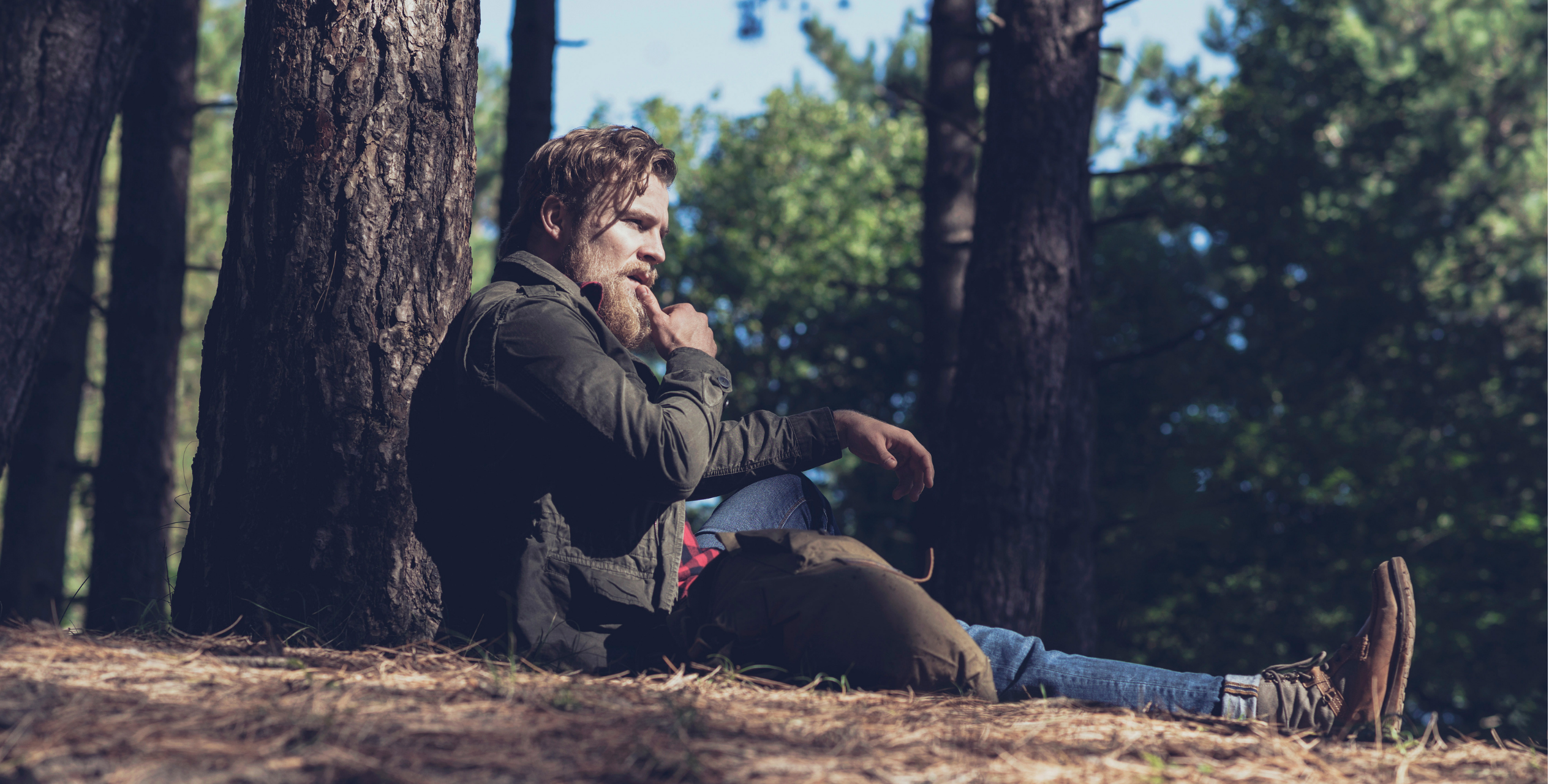 Man sitting against a tree in a forest, deep in thought, symbolising reflection and self-awareness